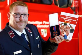 Chronik bringt das Feuerwehr-Ehrenkreuz - Mario Legies mit seinem Feuerwehr-Ehrenkreuz und der Chronik, die er zusammen mit anderen Feuerwehrleuten verfasst hat.