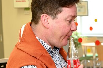 Colaflasche statt Querflöte: Freiberger Montessori-Kinder sind begeistert - Musiker Sören Glaser demonstriert mit einer leeren Colaflasche in Freiberg, wie er in die Flöte blasen muss, damit ein Ton entsteht.