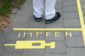 Corona-Impfung: Ein Mann steht an einem Covid-19-Impfcenter hinter der Bodenaufschrift "Impfen".