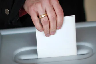 Eine Person wirft in einem Wahllokal den Stimmzettel in eine Wahlurne.