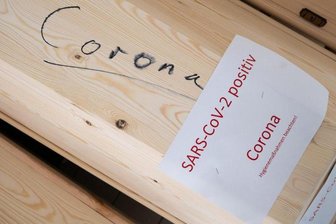           Särge mit Aufschrift "Corona" und "SARS-CoV-2 positiv - Corona" stehen in einer Kühlkammer.