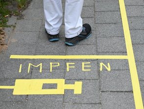 Ein Mann steht am Covid-19 Impfcenter hinter einer Bodenmarkierung mit der Aufschrift "Impfen" und einer Spritze.