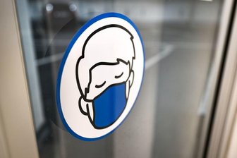 Ein Aufkleber an einer Glastür weist auf das Tragen einer Maske hin.