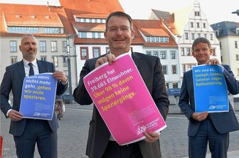 Corona-Proteste: So will Freiberg das angekratzte Image polieren - Plakat-Aktion: Mit Sprüchen wie diesen will die Stadt Freiberg dasdurch Protest-Spaziergänge angekratzte Image der Bergstadt aufpolieren. Urs Peuker (l.), stellvertretend für die TU Bergakademie Freiberg und Gunter Erfurt, stellvertretend für die ortsansässige Industrie, stehen hinter der Kampagne von OB Sven Krüger (M.)