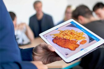 Das digitale Klassenzimmer - Jasin Peña Cabrera, Englischlehrer am Gymnasium Carolinum, unterrichtet mit Hilfe eines I-Pads, auf dessen Bildschirm ein paniertes Schnitzel mit Pommes frites zu sehen ist. Die Schüler werden so angeregt, auf Englisch über ihr Lieblingsessen zu diskutieren.
