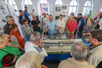 „Das Flugplatzfest war ein Highlight“: Wie Chemnitz sich an seinen Flughafen erinnert - Organisator Andreas Hütter (Mitte im blauen Hemd) erläutert ein Modell des Chemnitzer Flughafens in der Ausstellung anlässlich des 100-jährigen Jubiläums.