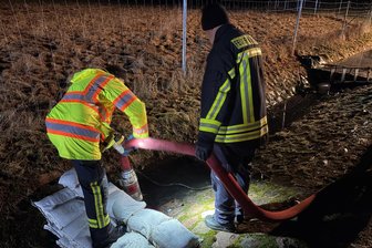 „Das ist eine Sauerei“: Bürgermeister im Erzgebirge schimpft über Umweltfrevel - Einsatzkräfte pumpen in Aue eine dunkle Flüssigkeit aus einem Graben ab und sichern den Bereich mit Sandsäcken, um eine weitere Ausbreitung zu verhindern.