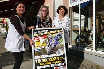 Das sind die Neuerungen bei „Rund um Zschopau“ - Vor dem Sanitätshaus-Schaufenster, das im Stile des Geländesports geschmückt wurde, platzieren Nicole Keil, Maria Goth und Katharina Beyer (von links) den Aufsteller samt Plakat.