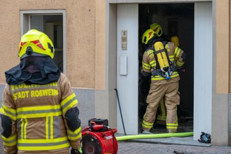 Defekt in Elektroinstallation: Zwei Verletzte nach Wohnhausbrand in Roßwein - Unter Atemschutz: Feuerwehrleute drangen in den verrauchten Hausflur der vor.