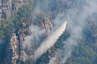 Der Brand in der Sächsischen Schweiz und seine Auswirkungen - Sachsen, Schmilka: Ein Lastenhubschrauber aus Österreich fliegt mit einem Löschwasser-Außenlastbehälter um einen Waldbrand im Nationalpark Sächsische Schweiz zu löschen.