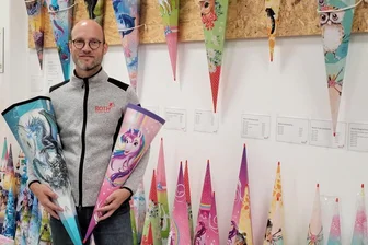 Der Herr der Zuckertüten: Ein Besuch in der Fabrik der Träume - Wie in einer Tropfsteinhöhle sind die Zuckertüten an der Wand aufgehängt. Lukas Roth, der Juniorchef der Lichtentanner Fabrik, zeigt zwei Tüten, die vor allem bei Mädchen in diesem Jahr hoch im Kurs stehen.