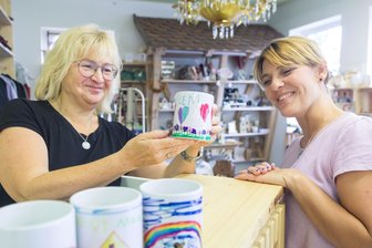 Der Laden im Laden: Wie ein Baugeschäft im Erzgebirge Kundinnen überrascht - Loreen Auerswald (r.) und Geschäftsinhaberin Carolin Böhm mit Tassen, die zum Oelsnitzer Stadtfest von Kindern bemalt wurden.