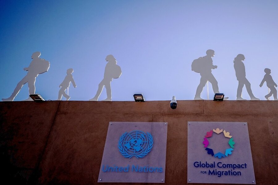 Der Pakt im Sand - Pakt für 285 Millionen Menschen: Der Aufsteller mit Silhouetten von Migranten weist auf die UN-Konferenz in Marrakesch hin.