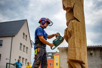 Der Riesenbergmann von Falkenau und die Geschichte des Bergbaus - Holzbildhauer Jörg Bäßler sägt aus einem Eichenstamm neben dem Falkenauer Volkshaus einen Bergmann. Der erste Tag sei der schwierigste, sagt Bäßler. Er müsse die Figur im Kopf fertig haben und sozusagen in den Stamm hineindenken und deshalb gut überlegen, bevor er die ersten Schnitte setzt. Es gibt nur drei Markierungen am Holz - für die Position der Füße, des Rumpfes und des Kopfes. Der Rest sei Handwerk, sagt er.