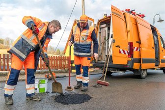 Der Schrecken der Straße: Warum so manche Schlaglochpiste im Erzgebirge als Filmkulisse herhalten könnte - Martin Windrich und Pierre Naundorf (v. l.) von der Straßenmeisterei Zöblitz bessern einen tiefen „Krater“ der Staatsstraße 221  in Mauersberg mit Kaltmischgut aus.