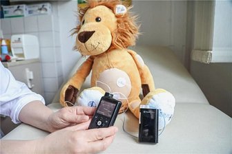 Diabetes im Kindesalter: Wie Kinder und Eltern mit der Krankheit umgehen lernen - Mit Löwe Lenny lernen Kleinkinder den Zucker in den Griff zu bekommen. Die Insulinpumpe, das schwarze Gerät, ist mit dem Katheter am Bauch verbunden. Sie gibt automatisch das benötigte Insulin ab.