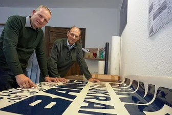 Die Beschriftungs-Spezialisten aus Bad Elster - Vor 30 Jahren gründete Wolfgang Röh (rechts) den Werbemarkt Röh in Bad Elster. Sein Sohn Thomas Röh stieg 2011 in das Geschäft ein und hat es im Jahr 2014 von seinem Vater übernommen. Das Bild zeigt beide an einem aktuell produzierten Aufkleber für die Oelsnitzer Firma Bang Kransysteme GmbH.