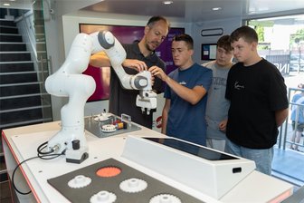 Die Reichenbacher Weinholdschule hat ein Platzproblem - wieder - Im Info-Truck der Metall- und Elektroindustrie. Michael Hoeffer zeigt den Weinhold-Neuntklässlern Henry Werner, Max Kroll und Chris Wunderlich, wie der Cobot - ein kollaborativ arbeitender Roboter - funktioniert.