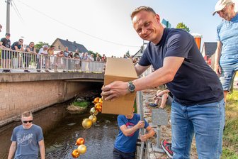 Dorf im Erzgebirge zelebriert mitten in der heißen Jahreszeit Weihnachten: Was ist da los? - Bürgermeister Stephan Weinrich schüttet eine volle Kiste Christbaumkugeln ins Wasser.