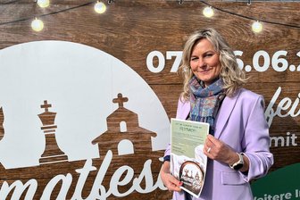 Drei Ortsjubiläen auf einmal: Ganz Grünhainichen feiert im Juni - Kristina Schubert, im Verwaltungsverband unter anderem für Kultur zuständig, vor einem der großen Banner, die auf das Heimatfest in Grünhainichen aufmerksam machen sollen.