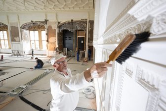 Dresdner Residenzschloss: Endspurt beim Jahrhundertprojekt - 19.05.2025, Sachsen, Dresden: Stuckateur Peter Schumann reinigt die Ostwand im Großen Ballsaal im Nordflügel des Dresdner Residenzschlosses mit einem Handbesen.