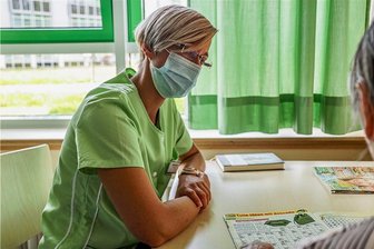 Ehrenamt im Krankenhaus Mittweida: Der Besuch der Grünen Dame - Die Grüne Dame Stefanie Jahr lässt sich im Krankenzimmer von Patientin Renate Baum ein Rätselheft erklären.