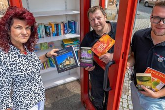 Eicher Telefonhäuschen kehrt nach Odyssee in die Heimat zurück - Auf dem Treuener Markt steht jetzt eine Büchertauschzelle. Bürgermeisterin Andrea Jedzig, ließ sich von den Kulturbanausen Maik Strauß und Lukas Lorber (rechts) zeigen, welche Bücher man dort finden kann.