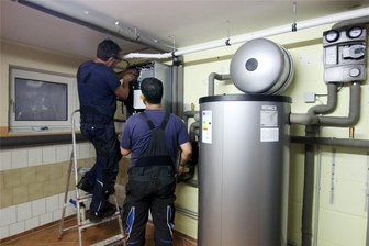 Ein Kommentar zum Heizungsgesetz: Vorsicht vor falschen Erwartungen - Zwei Handwerker stellen eine gerade installierte Wärmepumpe im Keller einer Doppelhaushälfte ein.