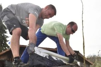 Eltern räumen verwilderten Garten - Ronny Vorwerg und Robert Müller (r.) tragen die Dachpappe von der Laube ab.