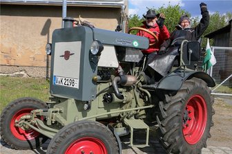 Ende der Coronazwangspause: Traktorenfans tuckern quer durchs Vogtland - Klaus Krause und Helga Ketzel winken auf ihrem Traktor der Marke Lanz Hermann. Sie waren aus Bad Elster angereist und hatten damit die weiteste Anreise aller Teilnehmer in Geilsdorf.