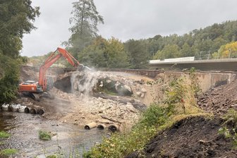 Ende einer Ära: Wernsdorf verabschiedet sich von einem Ingenieursmeisterwerk des 20. Jahrhunderts - Mit einer Hydraulikzange reißt ein Bagger den Beton der Straßenbrücke auf. Im Hintergrund die neu gebaute Brücke.