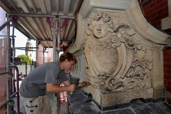 Endspurt bei Sanierung des Falkensteiner Rathauses beginnt, Zieleinlauf weiterhin offen - Nils Gruschwitz von der Firma Hollerung bei Restaurierungsarbeiten an der Fassade des Rathauses - das Relief zeigt den Engel mit dem Stadtwappen. Im Hintergrund der Turm der Kirche Zum Heiligen Kreuz.