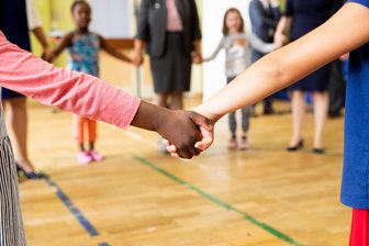 Ergebnis falscher Politik - Hand in Hand tanzen Kinder und Erzieherinnen bei einem Bewegungsspiel in der Turnhalle einer Kita. Der „Wohnort junger Menschen beeinflusst Chancen zur Teilhabe“. Foto: Christian Charisius/dpa