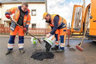 Erste Krater werden geflickt: So sieht es auf den Straßen im mittleren Erzgebirge aus - Martin Windrich und Pierre Naundorf (v. l.) von der Straßenmeisterei Zöblitz schließen einen tiefen „Krater“ in der Staatsstraße 221 in Mauersberg mit Kaltmischgut.