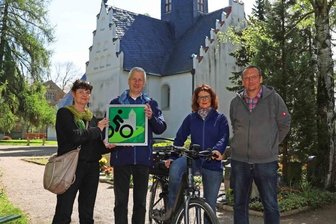 Erste Radwegekirche im Kreis lädt zum Verweilen ein - Kerstin Kracht überreichte Pfarrer Joachim Escher vor dem Langenhessener Gotteshaus das Signet "Radwegekirche". Ortsvorsteherin Jana Russ und Gunter Prem vom Kirchenvorstand waren dabei. 