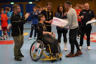 Erzgebirge Aue: Rollstuhlbasketballer profitieren von 105 Toren der Fußballtalente - Symbolischer Scheck: Die Rollstuhlbasketballer aus Zschorlau freuen sich über 1500 Euro.