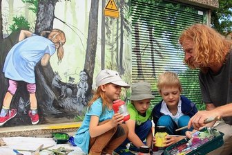 Fabelwelt aus Farbe ziert Limbacher Trafohäuschen - Mathilda, die für das Mädchen auf dem Bild Modell stand, und ihre Freunde Nevio und Vasco (von links) durften Dirk Söllner über die Schulter schauen und sich erklären lassen, wie Farben gemischt werden.