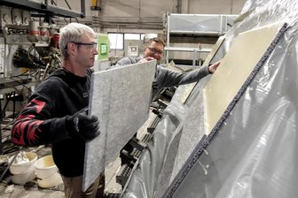 Fassaden-Spezialist aus dem Vogtland gibt gebrauchten Naturstein-Platten eine Zukunft - Jens Kunz (vorn) legt eine dünne Natursteinplatte auf die mit Kleber bestrichene Trägerplatte aus Leichtbeton. In der Vakuumpresse werden die Elemente felsenfest verbunden. Das System ist nicht nur federleicht, auch alle Formen und Formate sind möglich.