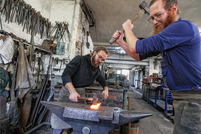 Feuer und Flamme für die Schmiedekunst - Die beiden Mitarbeiter Niko Kaiser und Thomas Böttcher von der Burgstädter Metallbau und Kunstschmiede Koch bearbeiten auf dem Amboss ein Stück Stahl für einen Pflanzstab. 