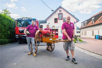 Floriansfest der Feuerwehr Adorf: Warum die Kameraden extra einen Termin beim Schneider hatten - Wehrleiter Rico Bochmann, Uwe Neuber und Tino Hofmann vom Feuerwehrförderverein Adorf mit dem sanierten historischen Löschwagen, der beim Floriansfest zu sehen sein wird.