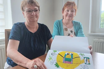 Gegen den Riss in der Gesellschaft: Wie die Partnerschaft für Demokratie Olbernhau das Zusammenleben fördert - Angela Klier (l.) und Katrin Schönherr zeigen ein Buch, das von der Partnerschaft für Demokratie Olbernhau und Umgebung verwirklicht wurde. Das Buch zeigt Malarbeiten von Kindern, die so ihre Erlebnisse aus der Coronapandemie verarbeiteten.
