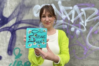 Geplante Liebesmauer in Zwickau: Disput mit Denkmalschutz beigelegt – Ärger wegen neuer Terrassen - Sara Linke mit dem Entwurf einer Liebeskachel. Im Hintergrund die derzeit beschmierte Wand, an der 450 solcher Kacheln angebracht werden sollen.