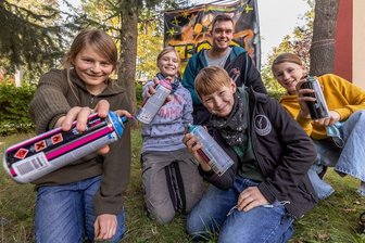 Graffiti machen Pappen und Folien lebendig - Schon die Band Keimzeit widmete Graffiti eine Liedzeile in ihrem Hit "Kling Klang". Graue Wände werden die Kinder und Jugendlichen, die sich an einem Ferienprojekt des Kreisjugendrings Erzgebirge beteiligen, nicht besprühen. Dafür aber Pappen und Folien. Denn was in manchen Fällen eher Vandalismus ist, kann auf der anderen Seite auch tolle Kunst sein. Wer könnte das besser wissen als Benjamin Knoblauch aus Niederwürschnitz - vielen auch unter seinem Künstlernamen Garlix Art bekannt. Mit Spraydosen verwandelt er Fassaden, Wände und vieles mehr in individuelle Kunstwerke. In der Alten Brauerei in Annaberg zeigt er den Teilnehmern des Graffiti-Workshops noch bis Mittwoch, wie aus einer Idee ein kunstvolles Graffito wird. Im Bild (v. l.): Kurt, Finja, Janne, Amrai und dahinter Benjamin Knoblauch.aed 