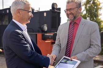 Gratulation an der neuen Schule auf Schienen - Auszeichnung vor einem ausgedienten Reisezugwagen, der in Neumark künftig der Ausbildung dient. Landrat Rolf Keil (links) beglückwünscht Schulleiter Sven Müller vom Johann-Heinrich-Pestalozzi-Gymnasium für das Engagement der Schule bei der Woche der offenen Unternehmen. 