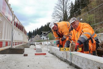 Großbaustelle im Erzgebirge: Am Schwarzwasser wird eine riesige Wand die Staatsstraße stützen - Heino Wolf (r.) und Ronny Gnatzy, Mitarbeiter der Firma Swing & Cut, beim Setzen von Bordsteinen auf der neuen Stützwand zwischen Schwarzwasser und Staatsstraße in Breitenbrunn.