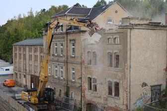Großer Bagger rückt in Aue an: Abrissarbeiten an Bahnhofsbrücke sorgen für Aufsehen - Bagger in Aktion: Der obere Bereich des Gebäudes unterhalb der Bahnhofsbrücke in Aue wird abgerissen.