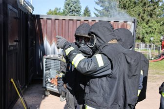 Härtetest für Feuerwehrleute: Warum drei junge Männer aus Fraureuth nur mit „Oma“ in die Feuerhölle dürfen - Mit der schweren Schutzausrüstung betreten die Feuerwehrleute aus Fraureuth den Container mit Hindernisparcours und brennenden Holzpaletten.