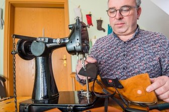 Handschuhmacher Rico Wappler hat etwas gegen kalte Finger - Handschuhmacher Rico Wappler an seiner Nähmaschine. Vor sich hat er einen der Spezialhandschuhe. Der Akku steckt hinter einem Reißverschluss an der Seite, das schwarze Band ist das Heizelement. 