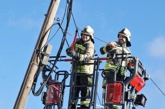 Havarie: Telefonmastgerät in Schieflage - Feuerwehrleute kappen die Leitung, damit der Telefonmast nicht auf die Straße stürzt.