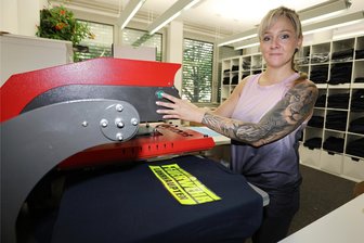Heiße Ware aus Kirchberg: Feuerwehrshop "Roter Hahn 112" hat, was Feuerwehrleute glücklich macht - „Roter Hahn“-Mitarbeiterin Diane Seidel bedruckt ein T-Shirt. Mit individuell gestalteter Kleidung für Feuerwehrleute ist das Kirchberger Unternehmen 2015 an den Start gegangen. Inzwischen reicht das Sortiment bis zu Geschenk- und Dekoartikeln wie Kaffeetassen, Taschen und Schwibbogen.